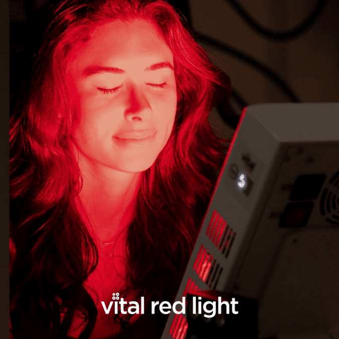 A person with long hair sits with eyes closed, bathed in the vital red light from a panel. The main text reads "vital red light," echoing the energy coursing through their tranquil pose.
