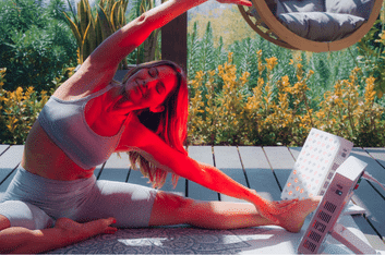 A woman in athletic wear stretches outdoors on a mat under panels highlighting the red light therapy benefits, with vibrant plants adding to the serene backdrop.