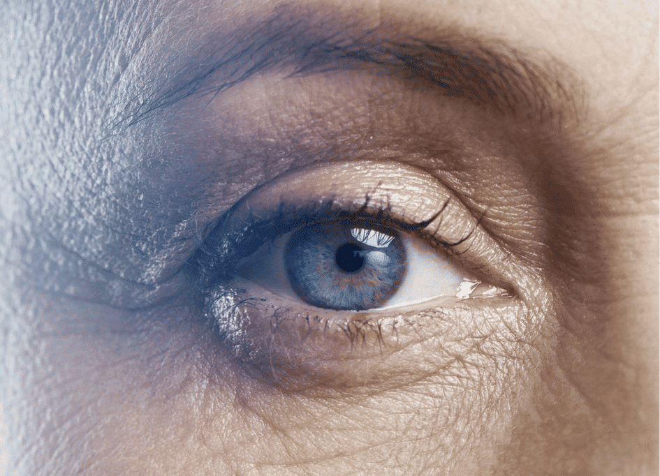 Close-up of a blue eye, showcasing detailed iris and surrounding skin texture, illuminated by gentle red light therapy for anti-aging benefits.