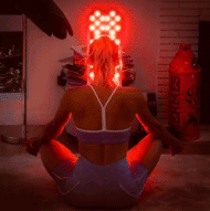 A person in workout attire sits cross-legged in front of a red light panel eager to witness red light therapy results.