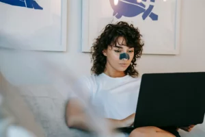 Person with a nose strip using a laptop on a couch, next to abstract art on the wall. Skin Type awareness and how its effected when in the sun