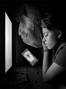 Person sleeping with head on a pillow beside an open laptop. A smartphone displaying a dog's image lies next to them. How light affects sleep
