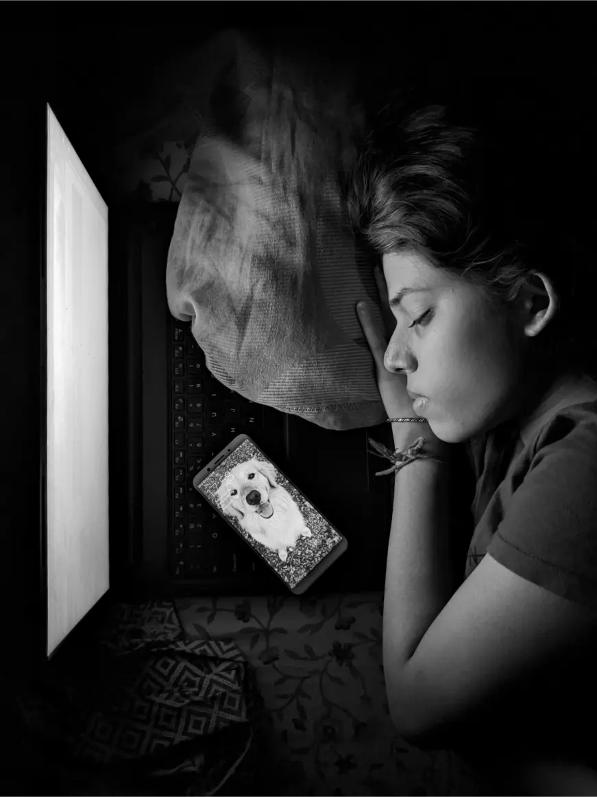 Person sleeping with head on a pillow beside an open laptop. A smartphone displaying a dog's image lies next to them. How light affects sleep